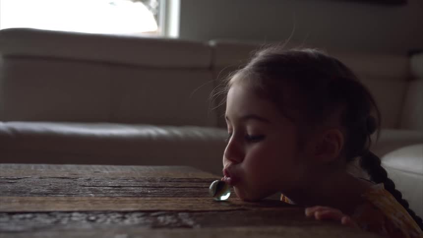 Little girl blowing and pushing a marble on a wooden table
