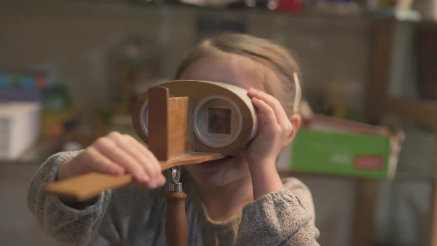 The little girl is holding binocular like toy up to her eyes and looking through it while laughing