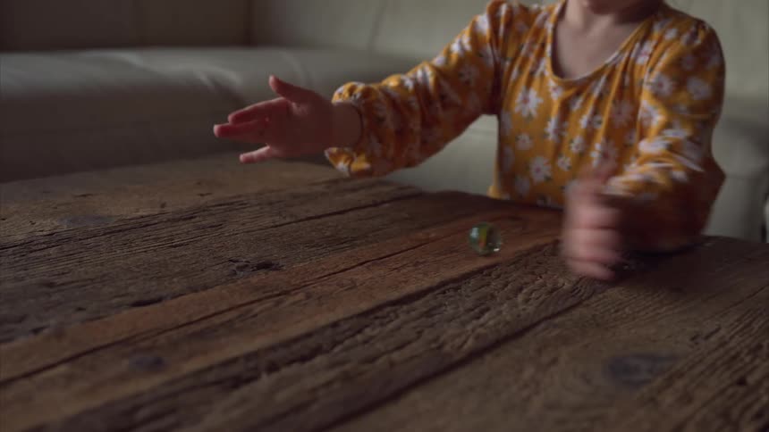 Little girl playing with a marble on a wooden table