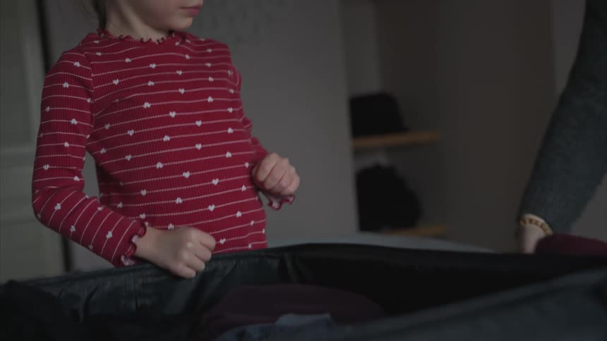 A girl and her mother are packing up a suitcase over the bed