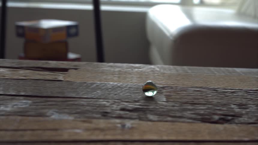 A young girl pushing a glass marble across a wooden coffee table in a living room during the day