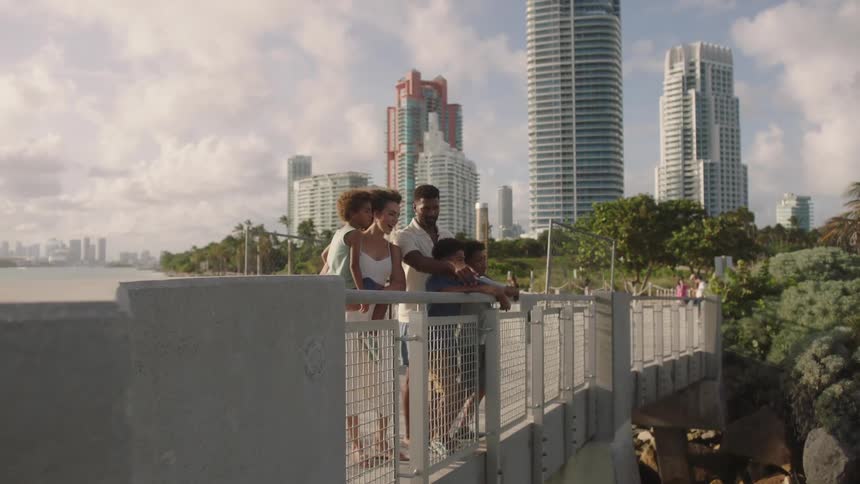 Family smiles while standing on a bridge with the skyline in the background on a cloudy day