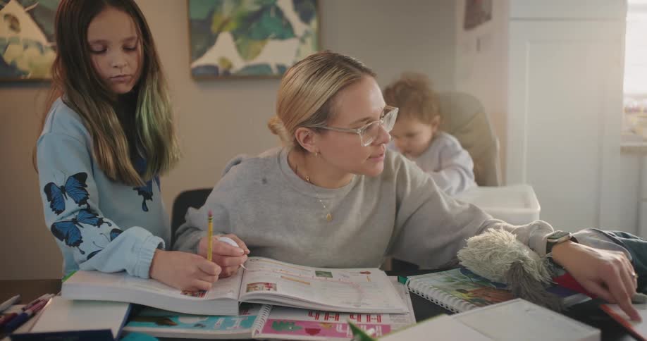 Mother studying with her young daughters with an open book on the table
