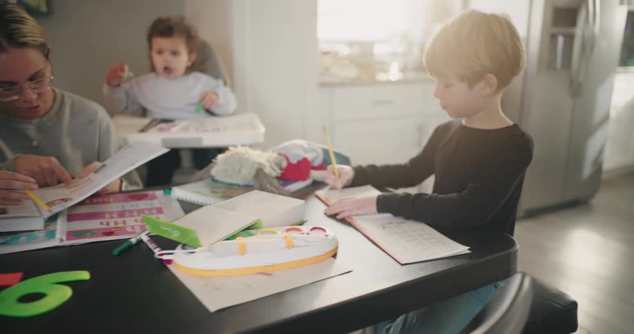 Mother sitting at the table with her three children around her playing and drawing