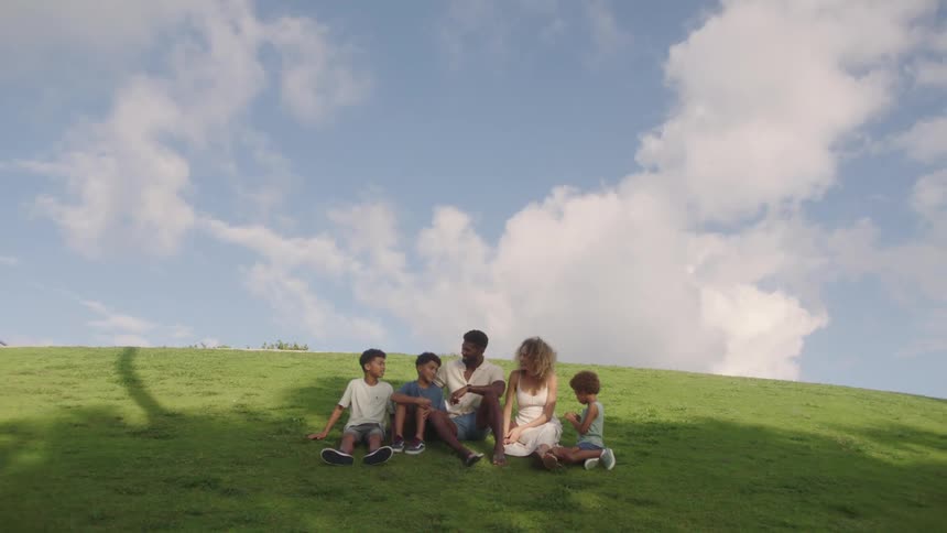 A family are talking while sitting on a green hill