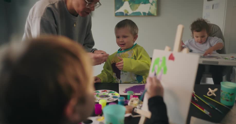 A mother is talking with her children as they paint