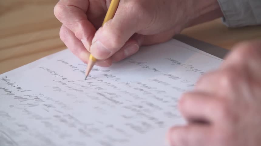A man writes on paper with a pencil