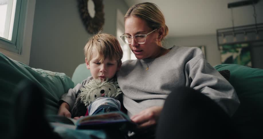 Mother and son sitting on a comfortable couch reading a book at home