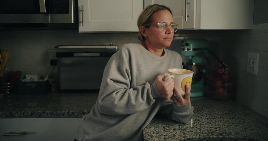 The woman is holding her coffer cup with both hands and is breathing deeply while looking towards something off screen