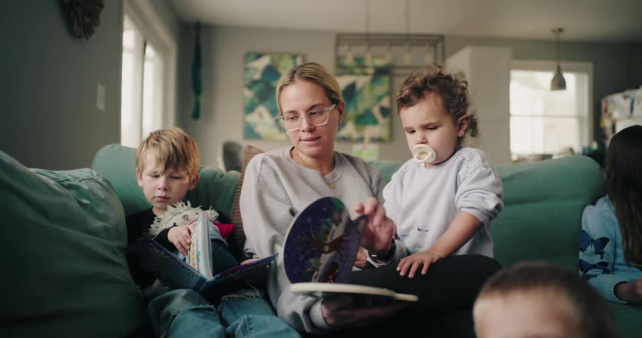 A mother and her children are reading books on the couch