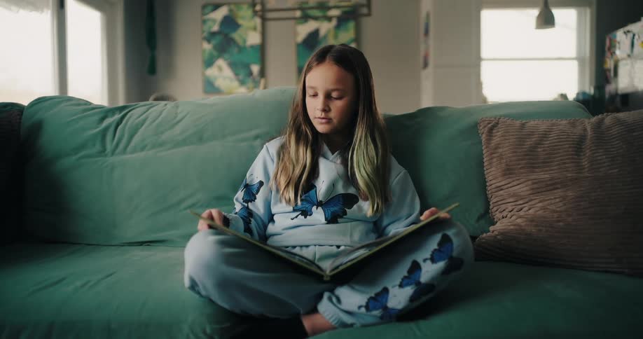 Blonde girl sitting on the couch in the living room reading a book