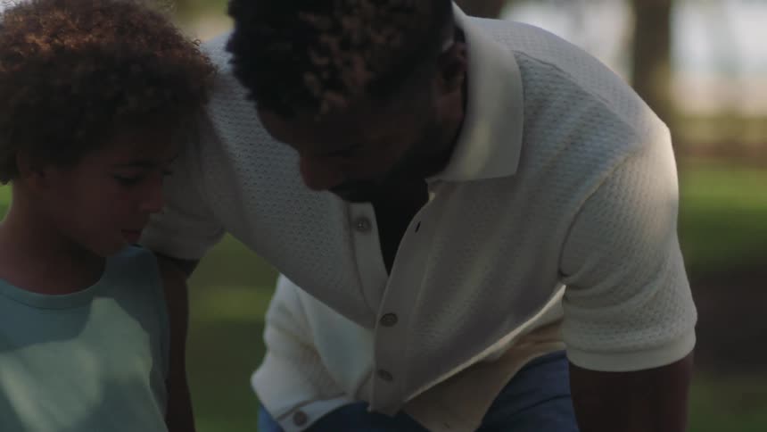 A father helping out his son to stand on a skateboard on a park