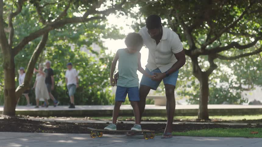 Father teaching his son how to skateboard at a park