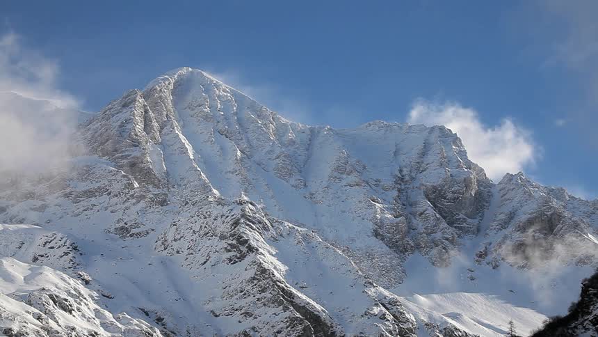 Light clouds hover over a snow-covered mountain top