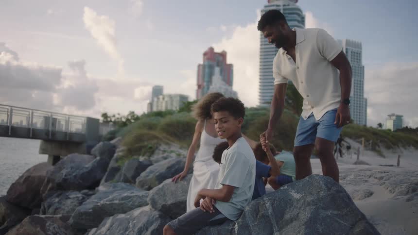 A family sit on the rocks by the shore