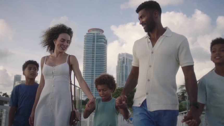 A family have fun walking on a bridge near a coastal city at dusk