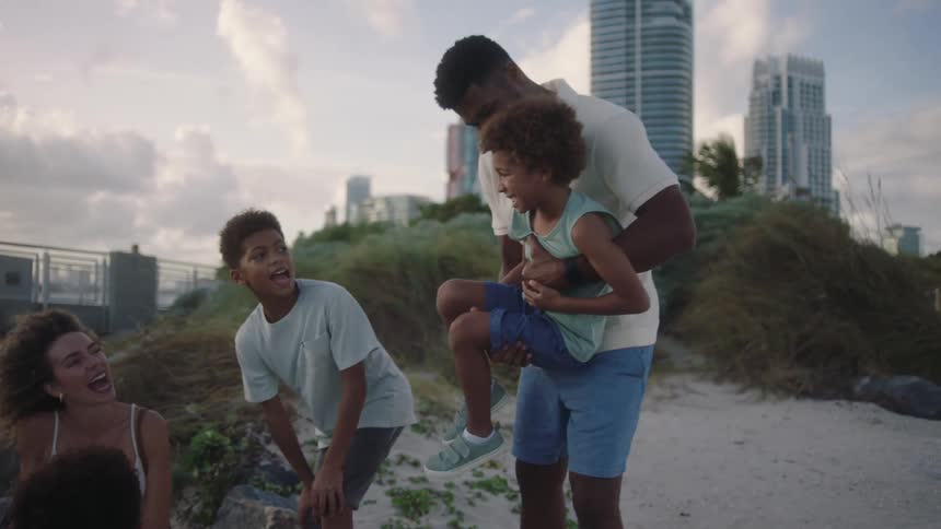 A family share a playful moment in a beach near a coastal city at sunset