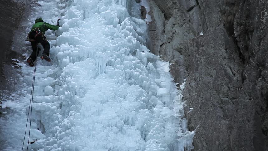 Man with ice picks climbing up an icy wall
