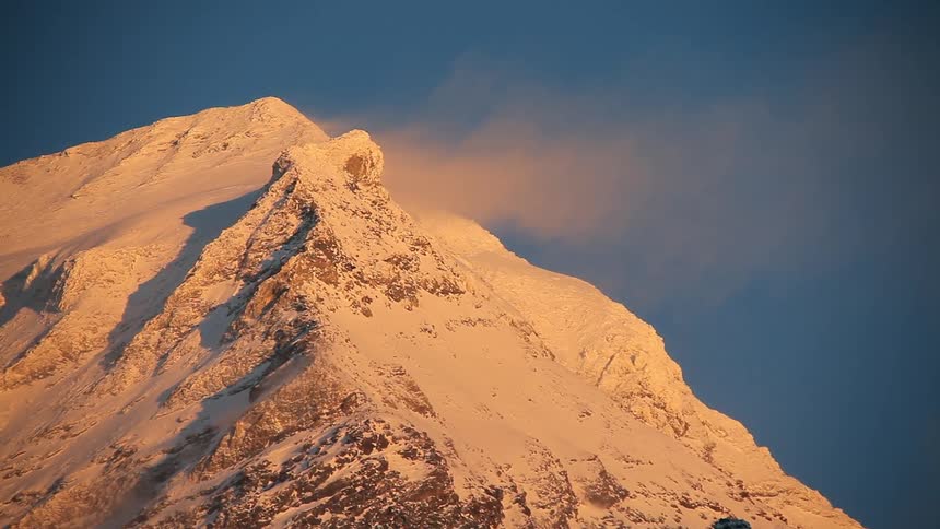Clouds floating next to a snow covered mountain top