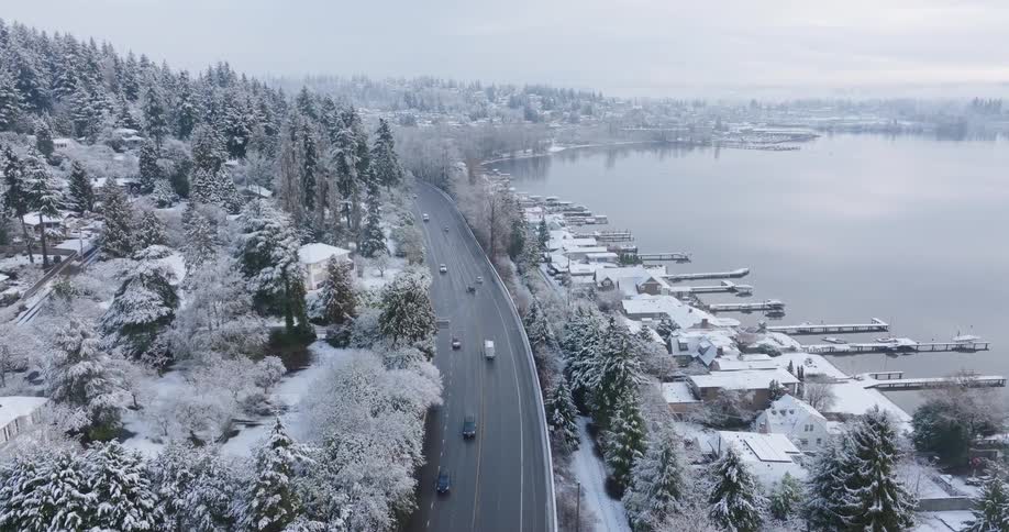 Tilt up traverse above highway traffic winding its way through a lakeside neighborhood dusted in snow