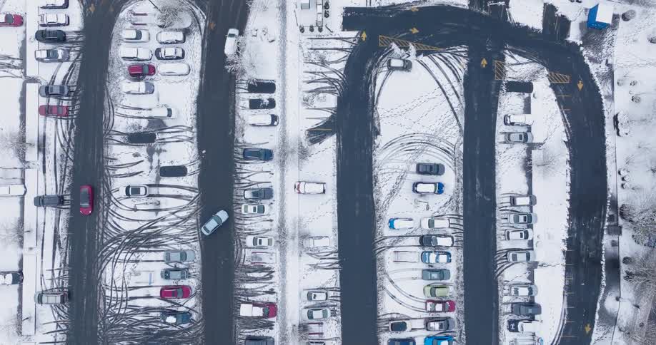 Vehicles slowly drive around a parking lot that is lightly covered with snow