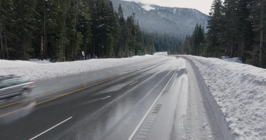 A pickup truck and car pass each other while leaving trails of mist along a slick and icy mountain highway