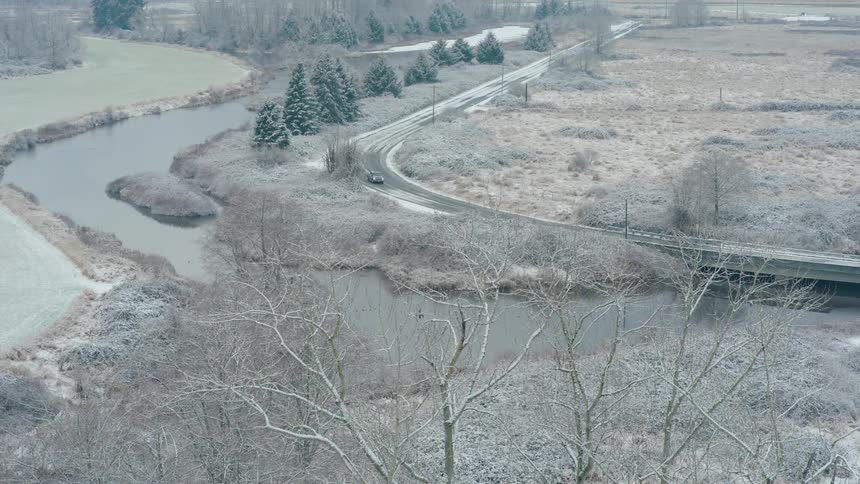 A heavy duty pickup drives carefully along the curve of an icy riverside road in winter weather