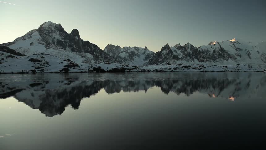 A lake reflects a snow-covered mountain range at dawn