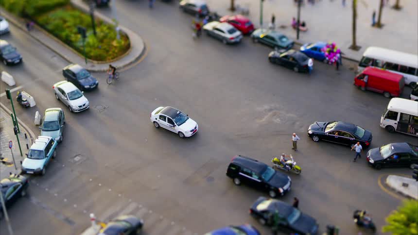 A bustling urban intersection features cars motorcycles bicycles and pedestrians navigating the area