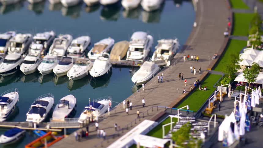 Pedestrians walk along the edge of a marina with yachts