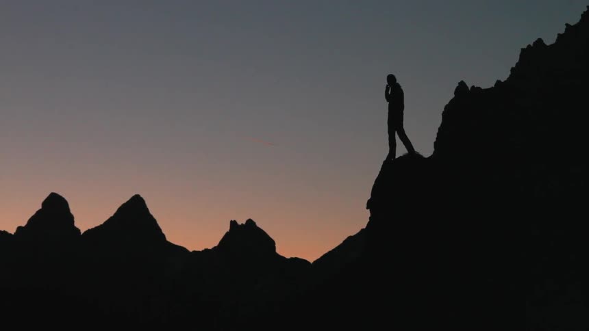 A man is standing on a rock ledge at dusk