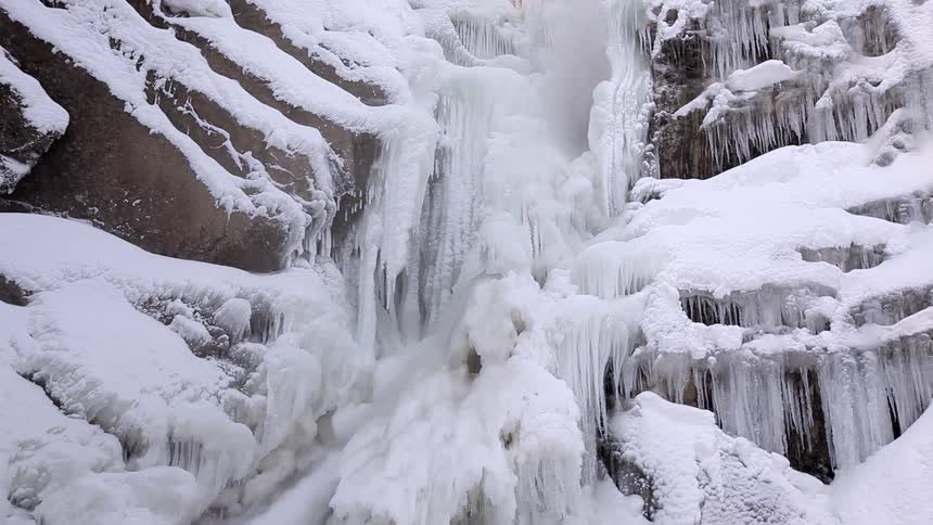 A waterfall flows over and under ice and snow