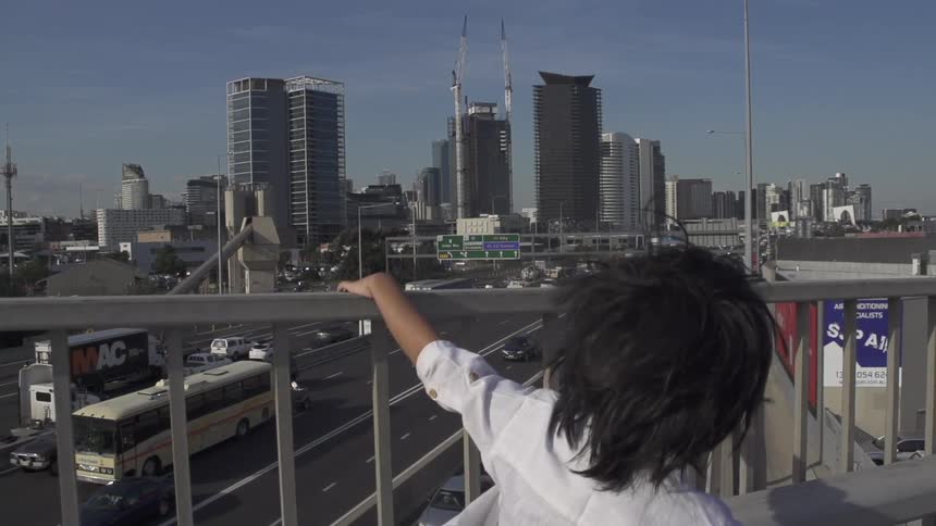 Child standing on an overpass watches vehicles drive down the highway