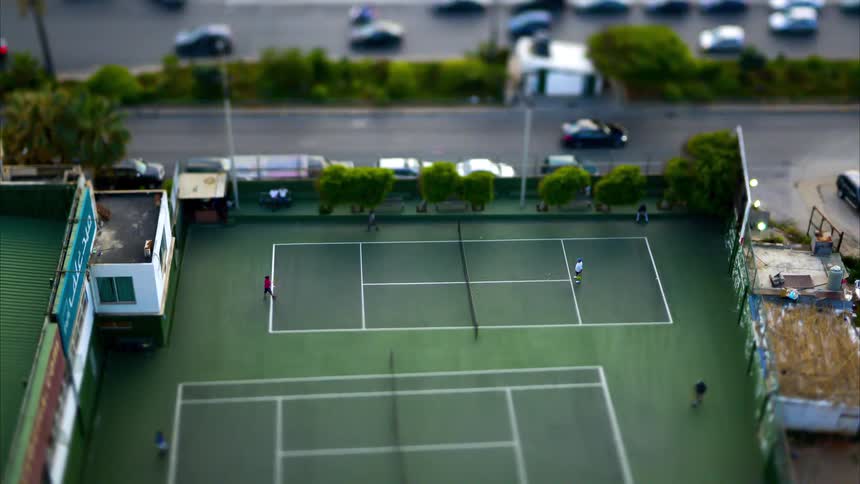 Aerial view of people playing tennis on a court next to a highway with traffic