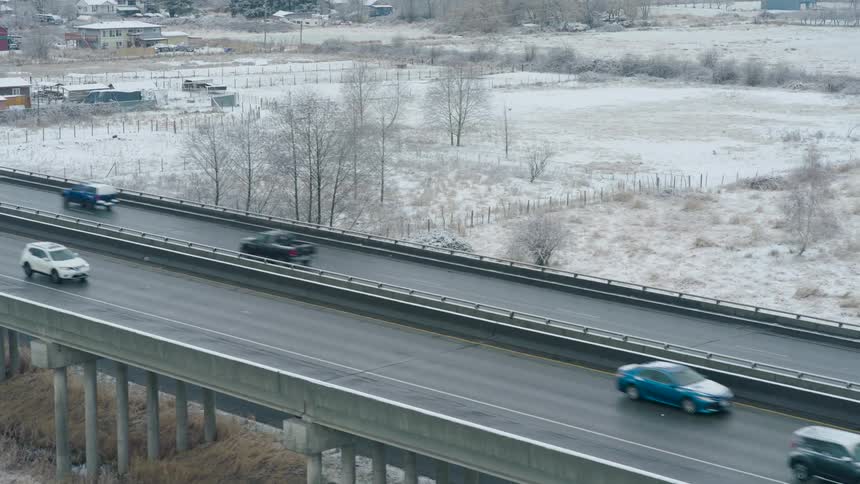 Vehicles travel on an elevated highway crossing a cold and snowy rural landscape