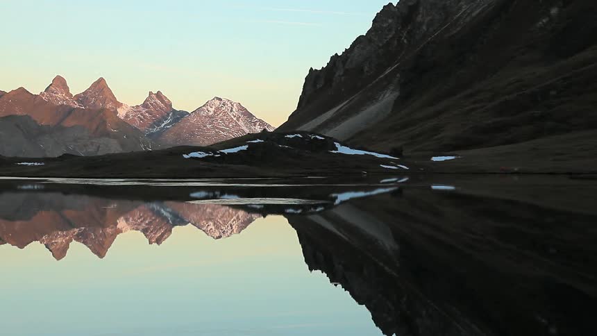 A lake reflects the surrounding mountains and blue sky