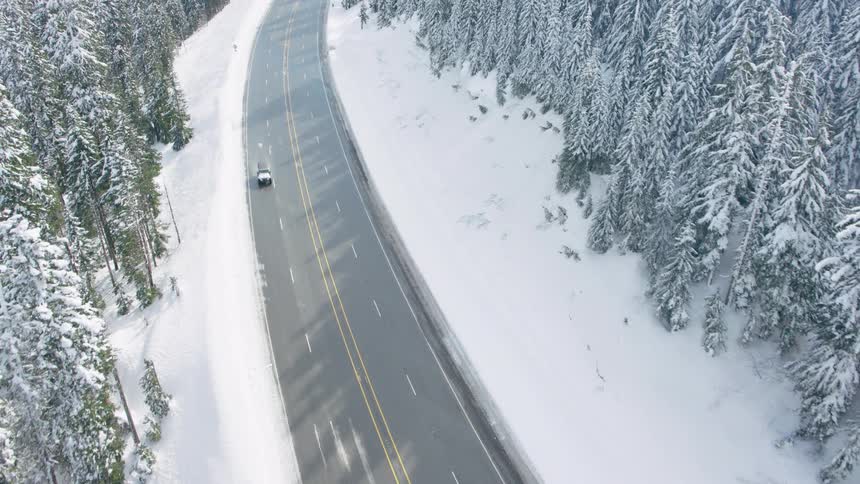 A SUV drives through puddles and slush on a mountain pass highway surrounded by deep snow