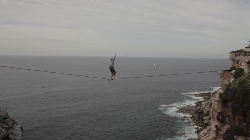 A person walks across a tight rope over top of ocean water