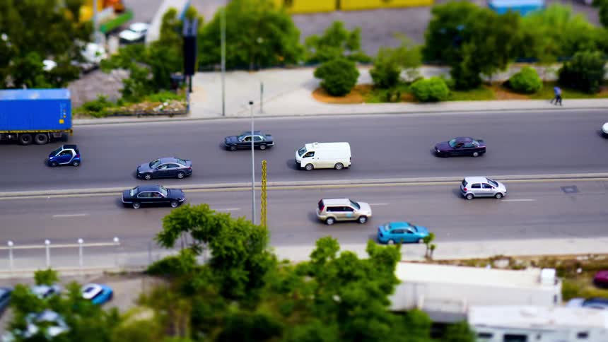 Traffic moving along a highway passes a parked vehicle on a summer day