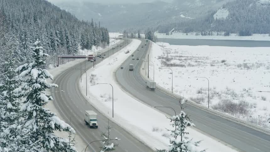 Cars are trucks travel on a damp and slushy interstate highway through a snowy mountain pass