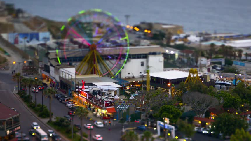A tiltshifted view of a ferris wheel in a coastal theme park