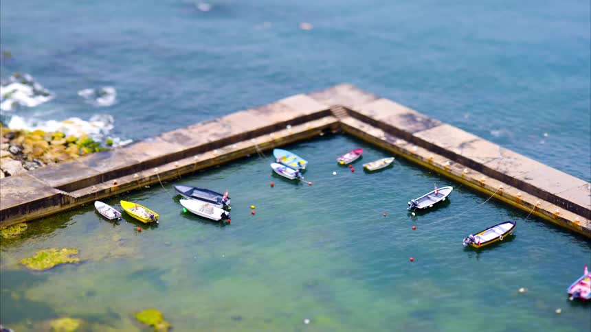 A small harbor enclosed by a stone pier where several colorful boats float in the clear turquoise water