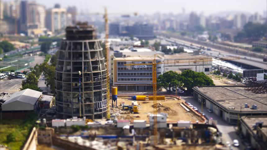 A tiltshift aerial view captures a construction site with a unique cylindrical building under construction surrounded by a cityscape and highways