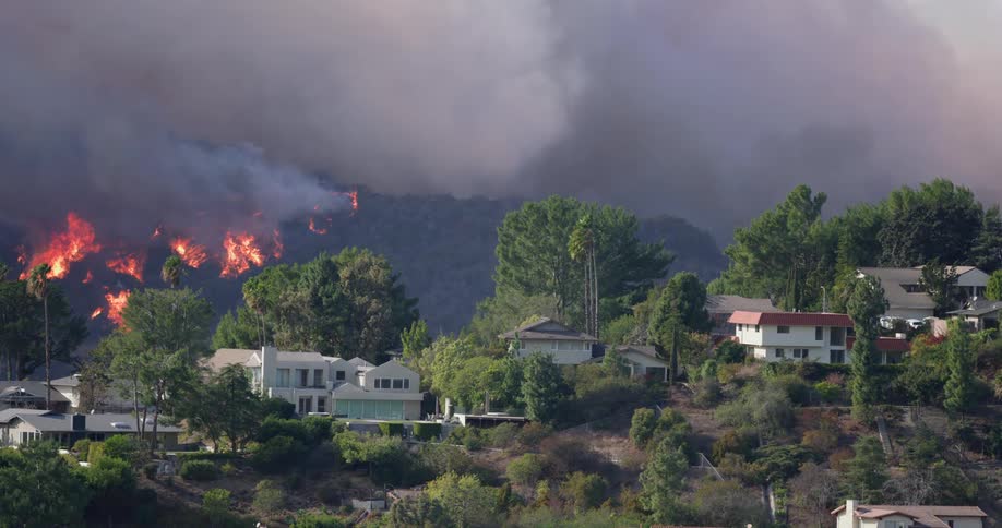 Flames engulf a hillside behind a residential neighborhood sending smoke billowing into the sky