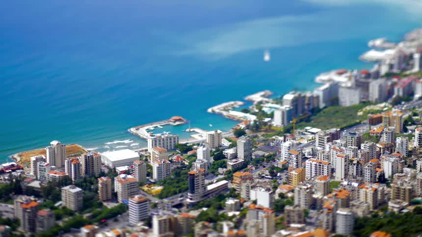 A tiltshift aerial view captures a densely packed city nestled along a coastline with a blue ocean