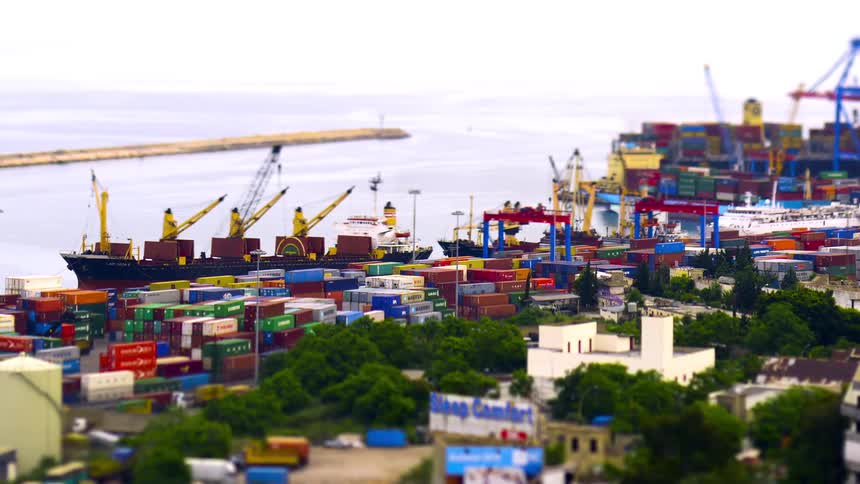 Trucks drive past busy docks while loading cranes load ships