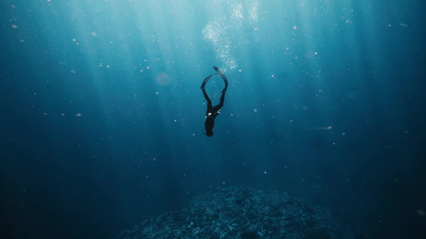 Diver diving towards coral underwater in the ocean