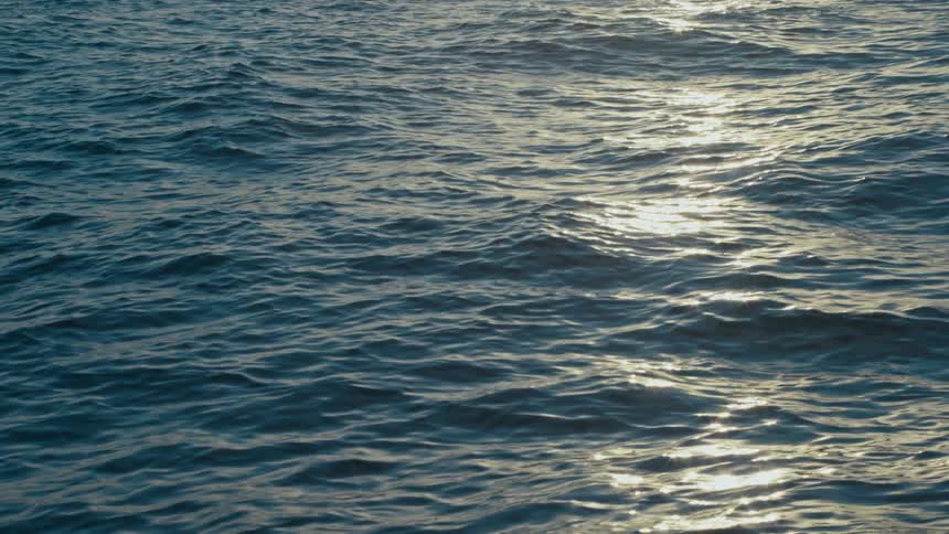 Sunlight is shining on ocean water while the waves move swiftly