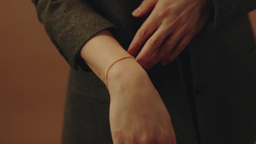 A person wearing a trench coat is adjusting a bracelet on their arm