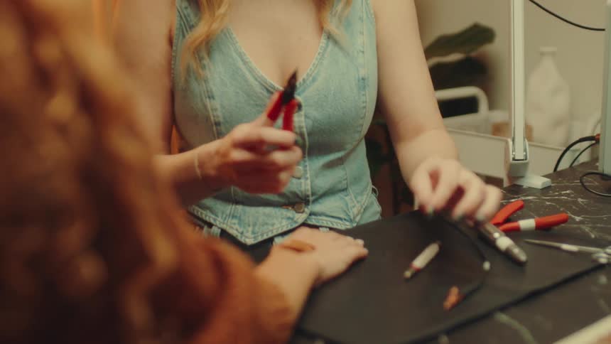 A woman adjusting small square brown leather piece beneath a gold chain on another persons wrist